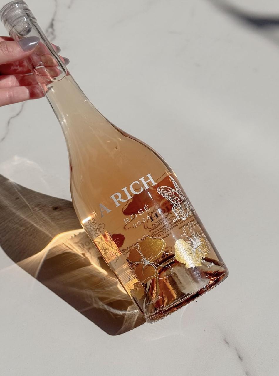 A hand holding a bottle of A Rich Rosé 2024 in golden sunlight on marble