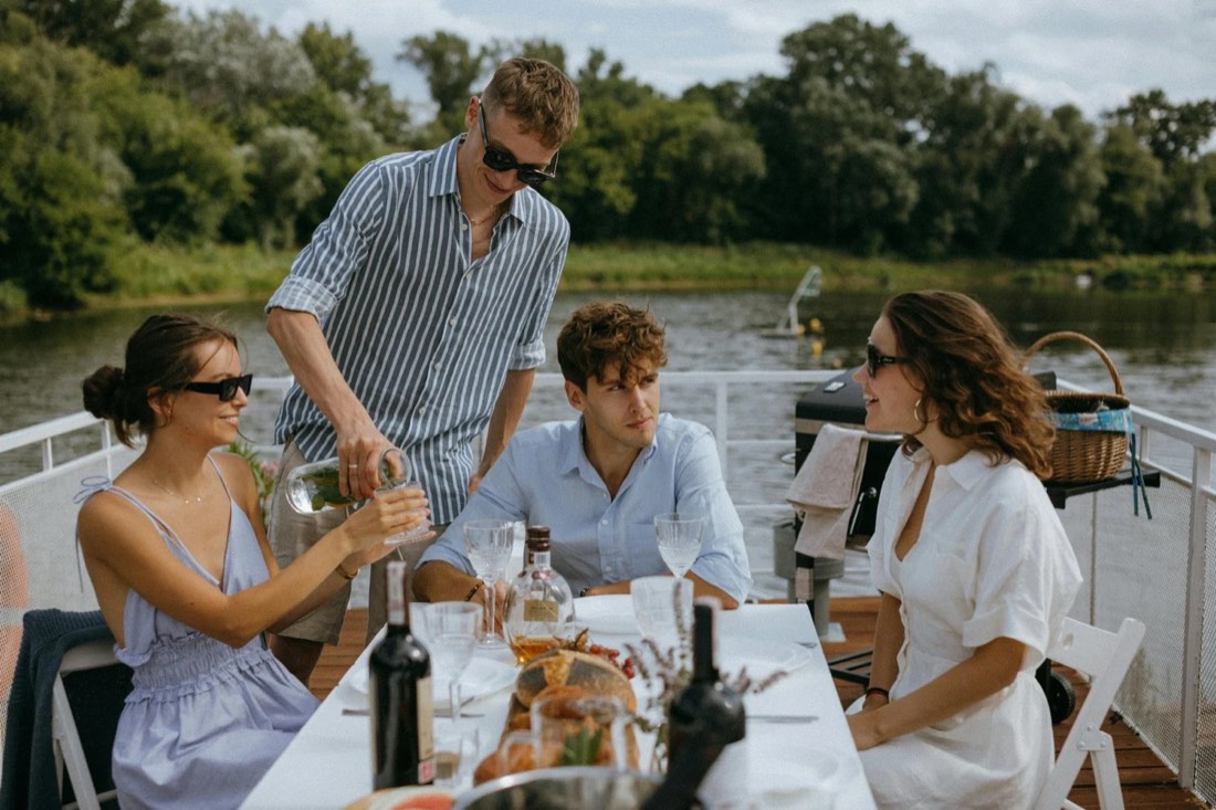 Friends pouring wine at a lakeside table on a boat deck