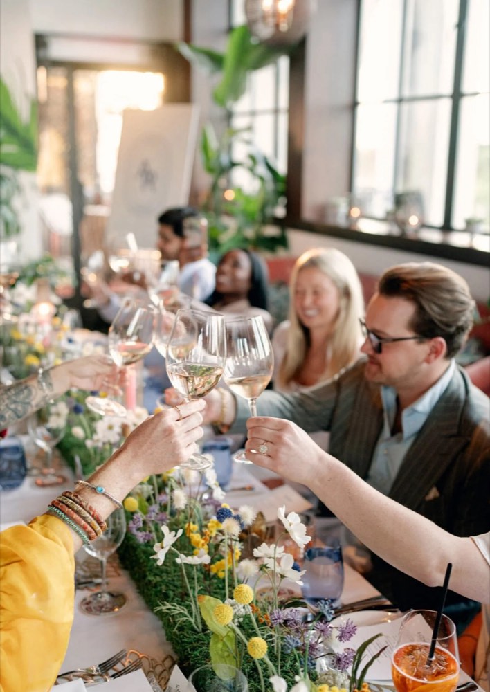 Guests raising glasses of rosé over a flower-lined table at an A Rich dinner